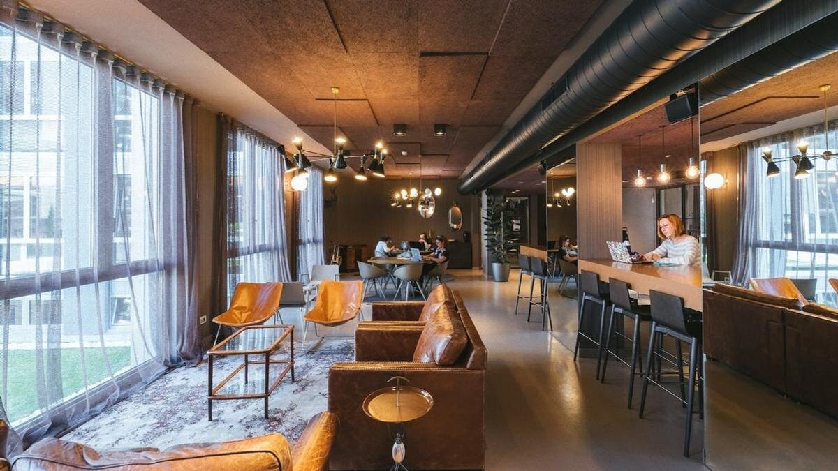    В просторном помещении стоят диваны, высокие стойки, стулья. В дальнем конце за столом сидят четыре человека, одна женщина работает с ноутбуком за стойкой:Unsplash/Copernico