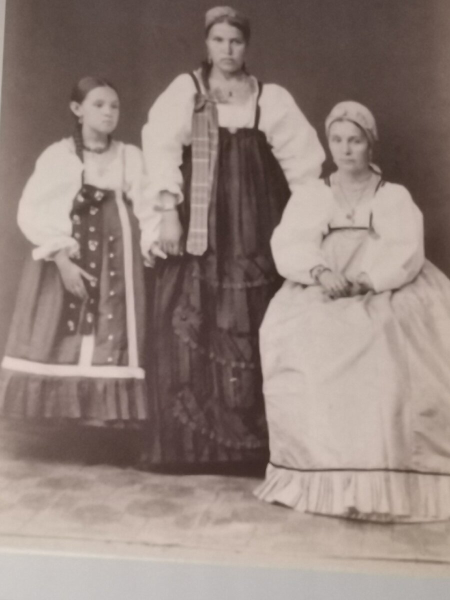 На фото женщины трёх поколений. Девочка, девушка и замужняя дама. Отличительная черта каждой - это волосы. Если одна коса и без ленты, то это девочка-ребенок. Если в косе есть лента, то у девушки есть жених. И чем выше лента, тем ближе свадьба. У замужних женщин уже две косы. Это говорит, что она в паре, их двое. И голова обязательно покрыта головным убором.