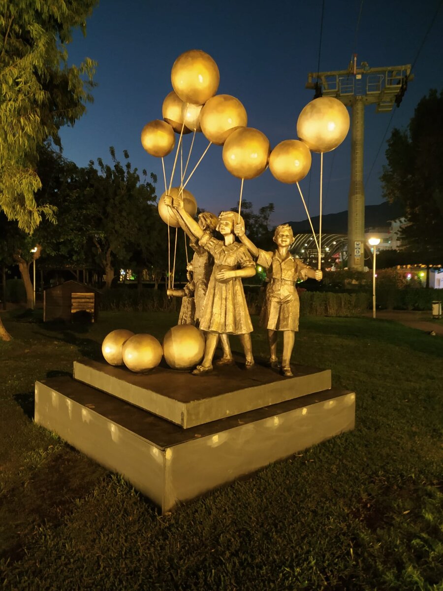 Счастливые, красиво одетые девочки и мальчики с шариками на верёвочках в руках. Учитывая материал создания (всё-таки это металл), выглядит очень изящно.