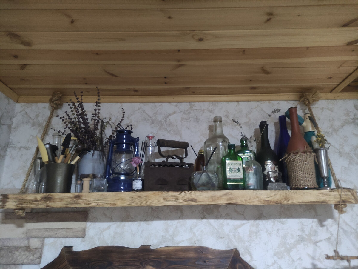 Массивная, деревянная полка над лестницей. На ней стоят старые красивые бутылки, пузырьки, утюг и т.д.