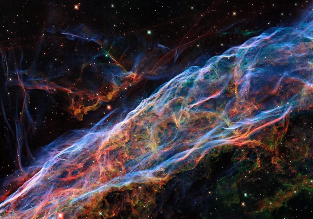    This Picture of the Week revisits the Veil Nebula, a popular subject for Hubble images! This object was featured in a previous Hubble photo release, but now new processing techniques have been applied, bringing out fine details of the nebula’s delicate threads and filaments of ionised gas. To create this colourful image, observations taken by Hubble's Wide Field Camera 3 instrument through 5 different filters were used. The new post-processing methods have further enhanced details of emissions from doubly ionised oxygen (seen here in blues), ionised hydrogen and ionised nitrogen (seen here in reds). The Veil Nebula lies around 2100 light-years from Earth in the constellation of Cygnus (The Swan), making it a relatively close neighbour in astronomical terms. Only a small portion of the nebula was captured in this image. The Veil Nebula is the visible portion of the nearby Cygnus Loop, a supernova remnant formed roughly 10 000 years ago by the death of a massive star. The Veil Nebula’s progenitor star — which was 20 times the mass of the Sun — lived fast and died young, ending its life in a cataclysmic release of energy. Despite this stellar violence, the shockwaves and debris from the supernova sculpted the Veil Nebula’s delicate tracery of ionised gas — creating a scene of surprising astronomical beauty. Александр Шереметьев