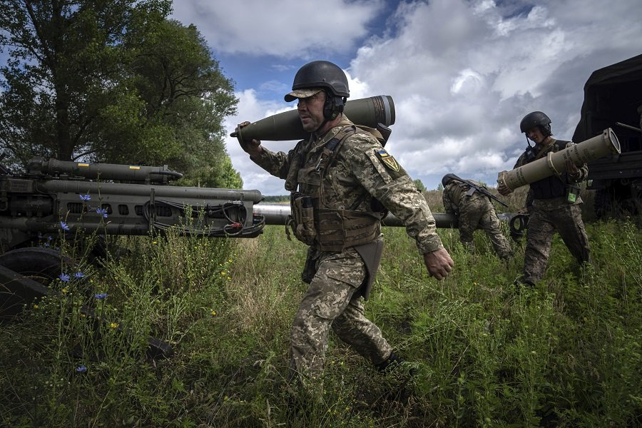 Украинский военнослужащий несет 155-мм артиллерийский снаряд, перед обстрелом российских позиций в Харьковской области из гаубицы M777 - Фото: Evgeniy Maloletka/AP/TASS