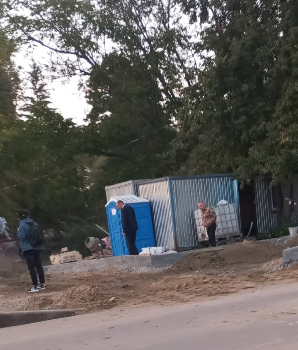 Сутулый мэр нашего округа контролирует работу на фоне синего туалета. 