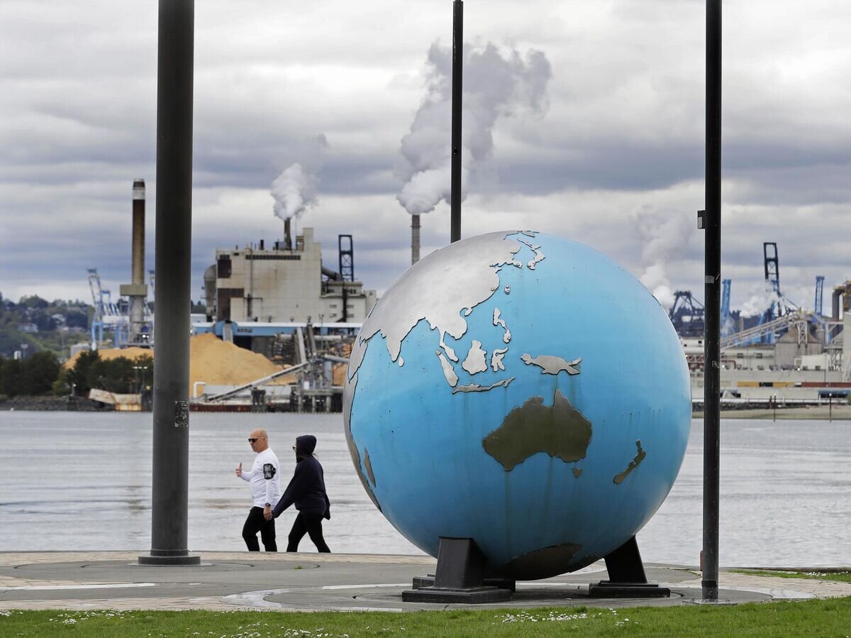    Люди проходят мимо скульптуры в виде земного шара на фоне фабрики © AP Photo / Ted S. Warren