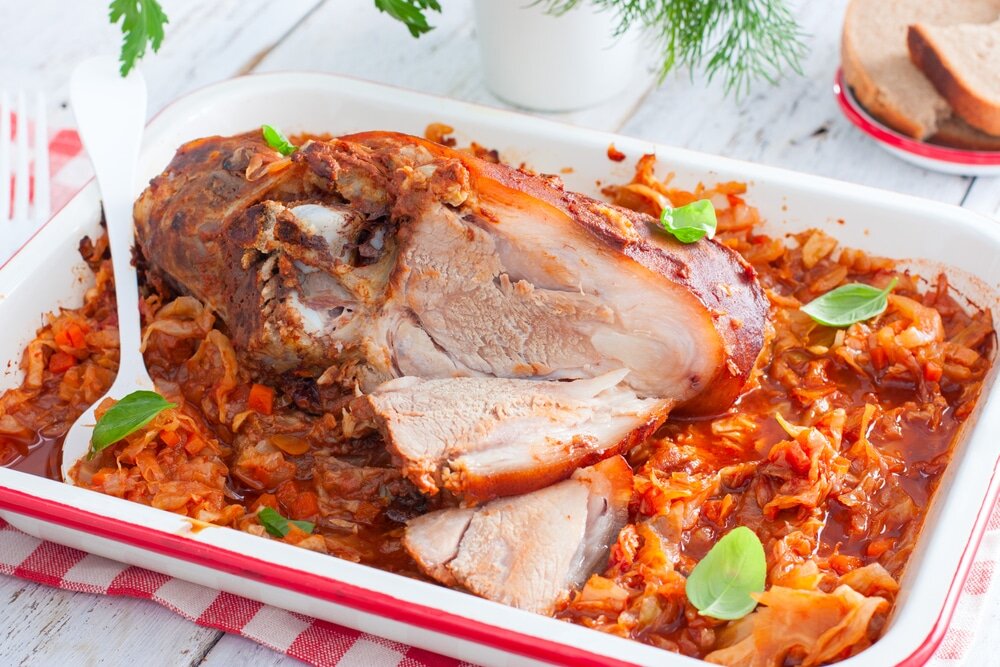 Ингредиенты: Свиная рулька - 1 шт
Горчица - 2 ст.л
Аджика - 2 ст.л
Томатная паста - 5 ст.л
Капуста белокочанная - Половина вилка
Морковь - 1 шт
Лук - 1 шт
Масло растительное - 2 ст.л

Приготовление:
1. Начнем, пожалуй, нашу работу с приготовления маринада. Смешаем вместе пасту томатную, острую аджику и разведенную горчицу. Мы получим довольно жгучий, но приятный на вкус соус. Свиную голень (рульку) хорошенько обмажем маринадом со всех сторон. Отложим в сторону.
2.  Шинкуем мелко морковку и лук. Выкладываем все в глубокую сковороду и обжариваем до легкой румяности.
3.  Накладываем в сковородку несколько ложек томатной пасты, продолжая жарить.
4.  Капусту необходимо нашинковать заранее, чтобы не прерывать процесс готовки. Бросаем ее в сковороду к луку и моркови. Тушим еще минут пять.
5.  После пережарки капусты с другими ингредиентами перекладываем все в форму, предназначенную для запекания в духовке. Сверху разместим свиную рульку и поставим печься в духовой шкаф.
6.  Выпекаем блюдо полтора часа. Можно два. Зависит от величины свиной голени, купленной вами.
7.  Готовое мясное блюдо можно подавать к столу не только по праздникам, но и в будни. 

Приятного аппетита!