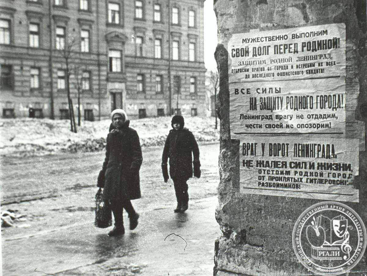 Плакаты «Мужественно выполним свой долг перед Родиной!», «Все силы на защиту родного города!», «Враг у ворот Ленинграда» на стене дома в блокадном Ленинграде. Фотография кадра из фильма «Ленинград в борьбе». 1942 г. РГАЛИ. Ф. 2989. Оп. 1. Ед. хр. 76. Л. 9. Фотокопия.