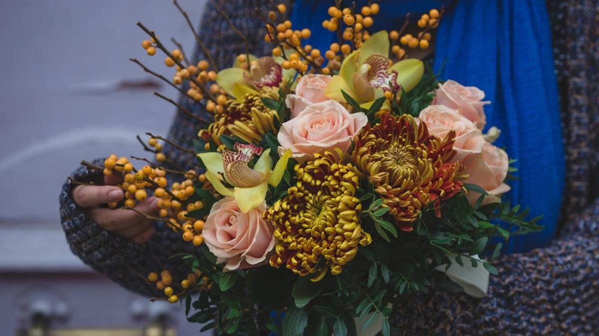    Женщина держит в руках зимний букет. Букет состоит из хризантем, роз, орхидей, зелени, облепихи:Freepik