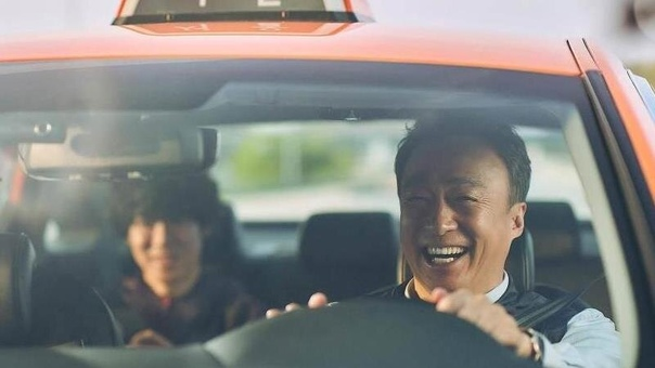 О Тхэк (Ли Сон Мин) улыбается, потому что не подозревает кого он везет и что ему предстоит пережить за эту поездку.