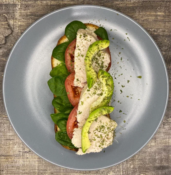 Бутерброд на бездрожжевом цельнозерновом кусочке хлеба с листиками шпината, спелыми томатами, курочкой и авокадо. 