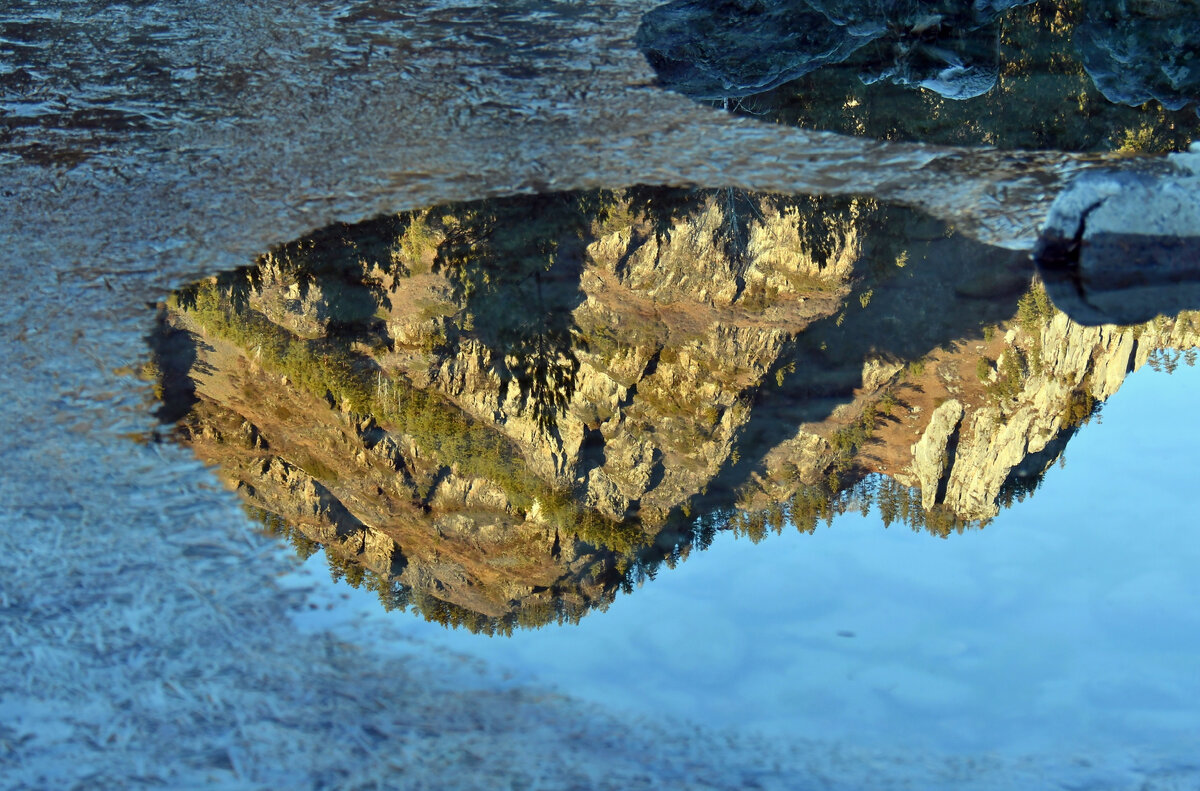 Отражение прибрежных скал, ярко освещенных предзакатным солнцем, и синего неба в заводи одного из Голубых озер.