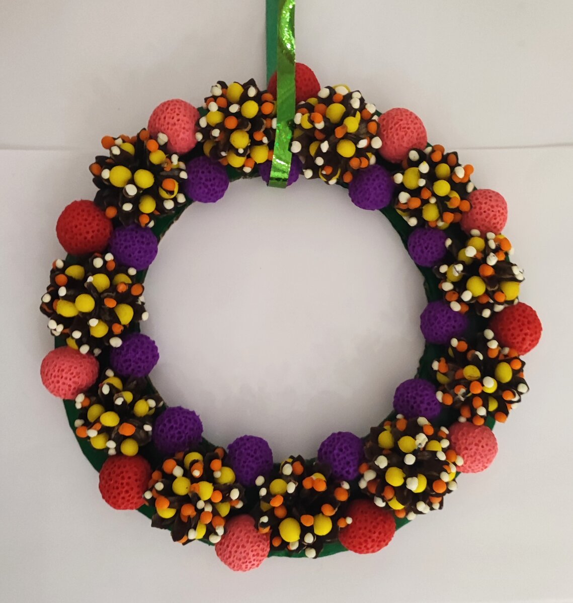 Готовый вариант рождественского венка из шишек и пластилина на картоне.