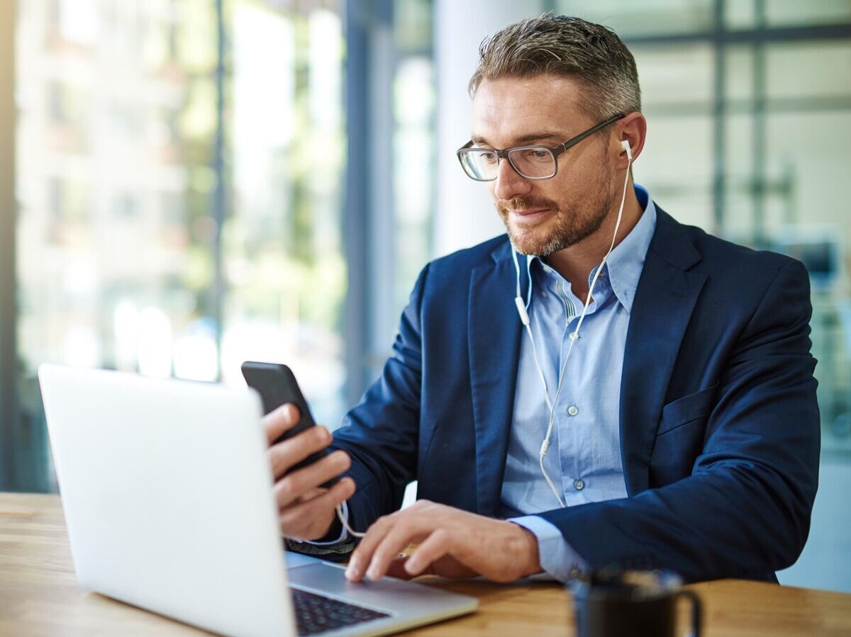    Мужчина использует смартфон и ноутбук в работе© iStock.com / Cecilie_Arcurs