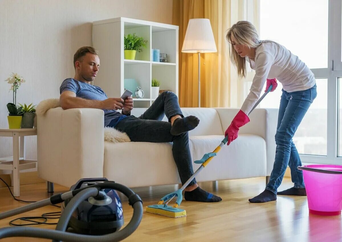 женщина пылесосит мужчина лежит на диване. видео жена работает. мужчина и женщина убираются. девушка флиртует с мужчиной. жена работает муж отдыхает.