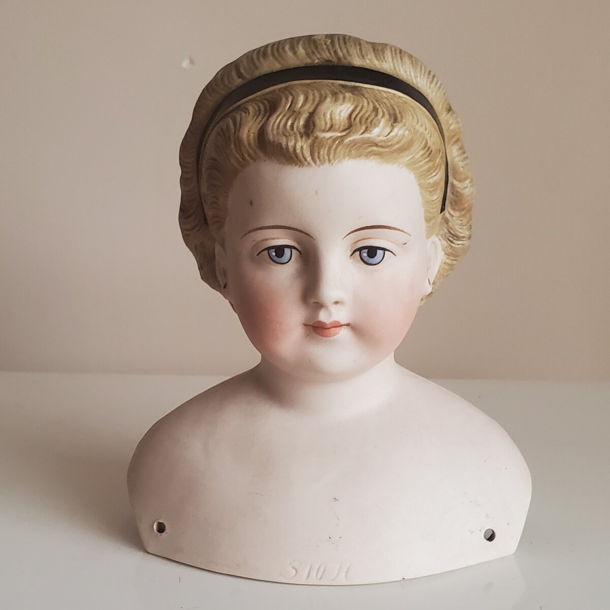 Фарфоровая антикварная кукла с формованным бюстом кукольной фабрики Simon&Halbig Германии, об этом свидетельствует клеймо на передней части декольте. Уши проколоты, без сережек. Цвет тела приближен к натуральному цвету. Фарфоровый бисквитный бюст антикварной куклы произведён в конце 19 века примерно 1875-1880 гг.  Она имеет маркировку в тесте S10H буквы означают начальные заглавные буквы фарфоровой фабрики Simon&Halbig. Фото автора.