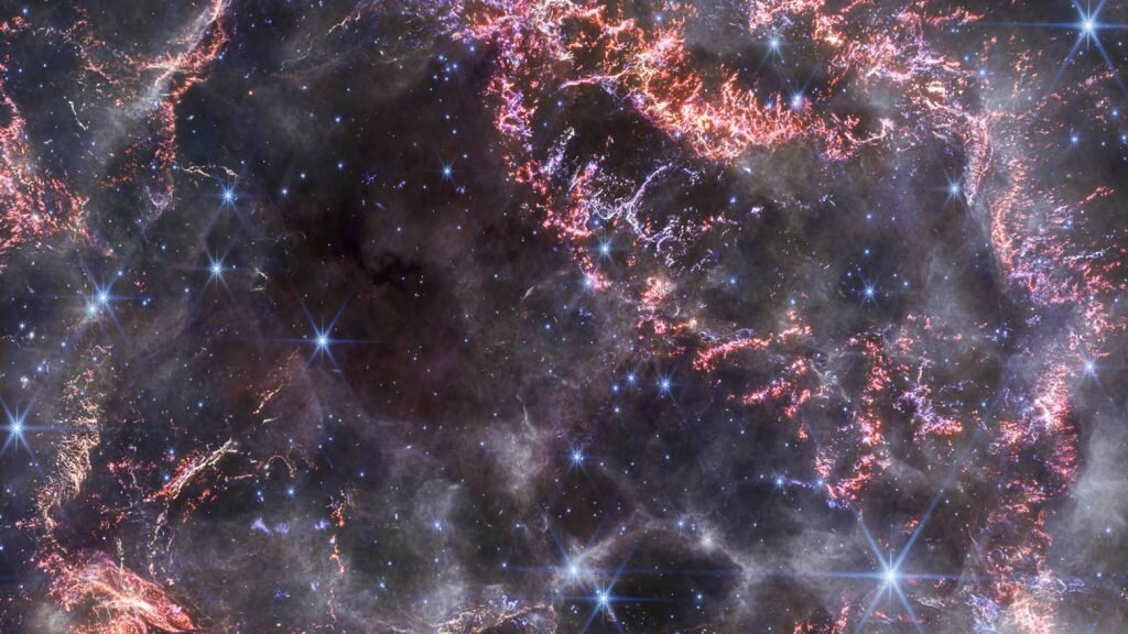    A new high-definition image from the NASA/ESA/CSA James Webb Space Telescope’s NIRCam (Near-Infrared Camera) unveils intricate details of supernova remnant Cassiopeia A (Cas A), and shows the expanding shell of material slamming into the gas shed by the star before it exploded. The most noticeable colours in Webb’s newest image are clumps of bright orange and light pink that make up the inner shell of the supernova remnant. These tiny knots of gas, composed of sulphur, oxygen, argon, and neon from the star itself, are only detectable thanks to NIRCam’s exquisite resolution, and give researchers a hint at how the dying star shattered like glass when it exploded. The outskirts of the main inner shell look like smoke from a campfire. This marks where ejected material from the exploded star is ramming into surrounding circumstellar material. Researchers have concluded that this white colour is light from synchrotron radiation, which is generated by charged particles travelling at extremely high speeds and spiralling around magnetic field lines. There are also several light echoes visible in this image, most notably in the bottom right corner. This is where light from the star’s long-ago explosion has reached, and is warming, distant dust, which glows as it cools down. [Image description: A roughly circular cloud of gas and dust with complex structure. The inner shell is made of bright pink and orange filaments studded with clumps and knots that look like tiny pieces of shattered glass. Around the exterior of the inner shell, there are curtains of wispy gas that look like campfire smoke. Around and within the nebula, various stars are seen as points of blue and white light. Outside the nebula, there are also clumps of dust, coloured yellow in the image.] Александр Шереметьев