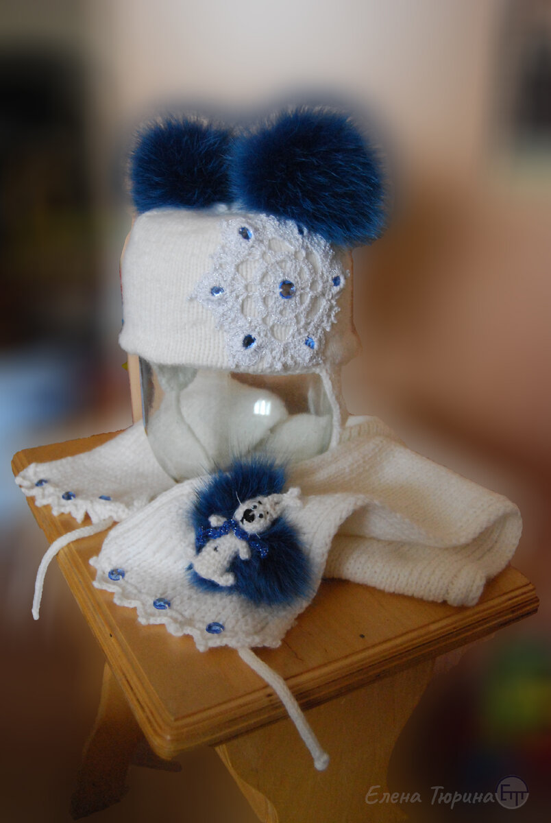 Дизайнер Елена Тюрина. Комплект шапка плюс шарф с вязанным зайчиком, декорированные стеклянными стразами, снежинкой, и меховыми помпонами.