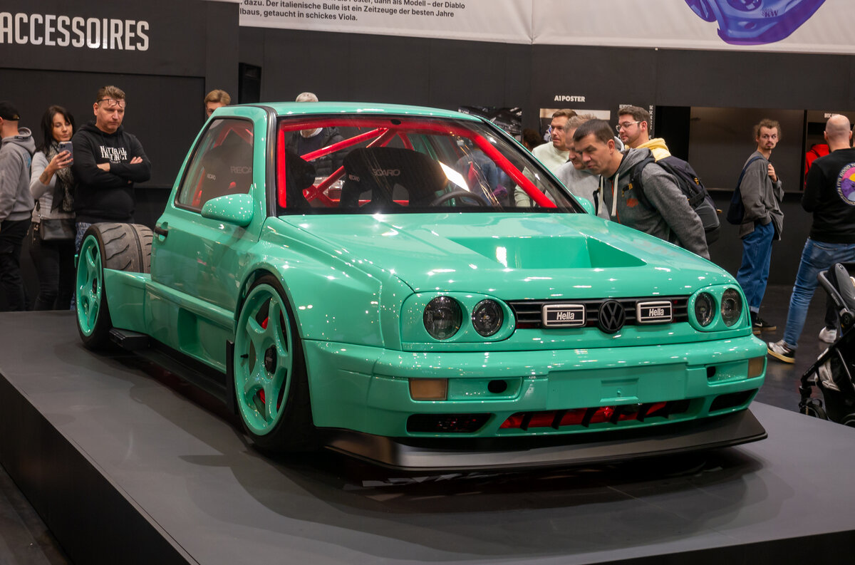    Автором главного шоу-стоппера в Эссене уже который год становится мастерская JP Performance местной телезвезды — ведущего реалити-шоу, а теперь популярного видеоблогера Жан-Пьера Кремера. Ребята из Дортмунда взялись за постройку отвязного проекта на основе Volkswagen Golf третьего поколения. Сразу скажем: от «Гольфа» там осталось немного — кузов распилили пополам, насадив на пространственную раму из стальных труб, также выполняющую функцию каркаса безопасности. Перед задней осью установили силовой агрегат от суперкара Audi R8 — двигатель V10 5.2 вместе с коробкой передач-«роботом» и системой полного привода. Но этим «Джей-Пи» не собирается ограничиваться: уже в ближайшее время его оборудуют парой турбин (на Audi RS6 C6 похожий турбомотор V10 развивал как миниум 579 л.с.). Двухрычажные подвески тоже собраны из компонентов Audi, регулируемые амортизаторы — фирмы KW suspension.   
Matti Blume / [Wikimedia](https://commons.wikimedia.org/wiki/File:EMS_2023,_Essen_(P1160940).jpg)