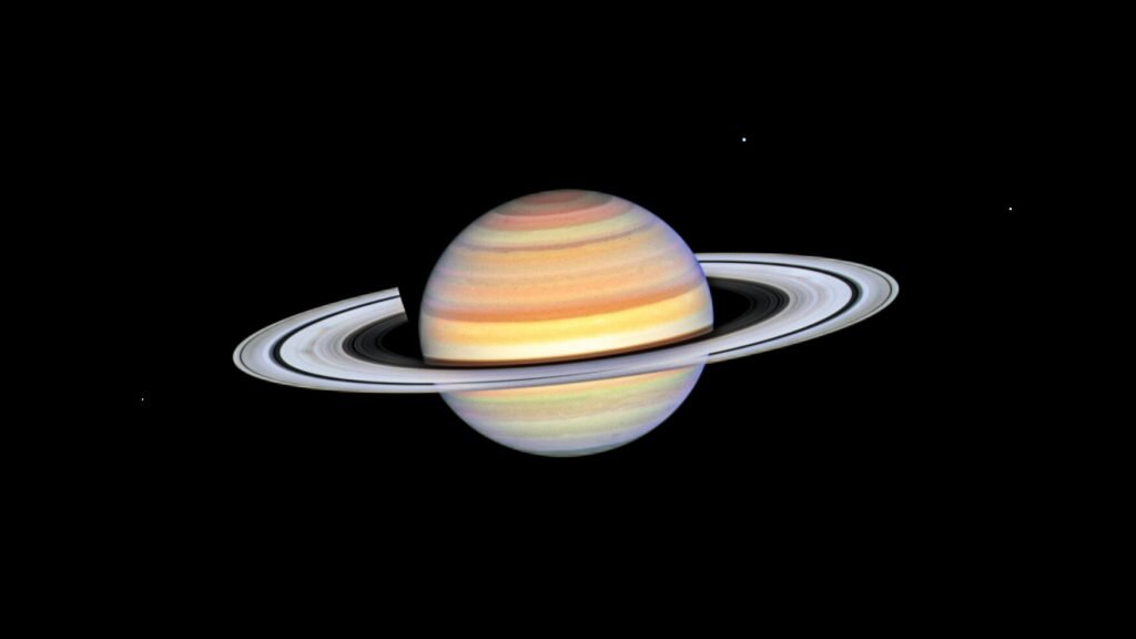    This photo of Saturn was taken by the NASA/ESA Hubble Space Telescope on 22 October 2023, when the ringed planet was approximately 1365 million kilometres from Earth. Hubble's ultra-sharp vision reveals a phenomenon called ring spokes. Saturn's spokes are transient features that rotate along with the rings. Their ghostly appearance only persists for two or three rotations around Saturn. During active periods, freshly-formed spokes continuously add to the pattern. In 1981, NASA's Voyager 2 first photographed the ring spokes. Hubble continues observing Saturn annually as the spokes come and go. This cycle has been captured by Hubble's Outer Planets Atmospheres Legacy (OPAL) program that began nearly a decade ago to annually monitor weather changes on all four gas-giant outer planets. Hubble's crisp images show that the frequency of spoke apparitions is seasonally driven, first appearing in OPAL data in 2021 but only on the morning (left) side of the rings. Long-term monitoring shows that both the number and contrast of the spokes vary with Saturn's seasons. Saturn is tilted on its axis like Earth and has seasons lasting approximately seven years. This year, these ephemeral structures appear on both sides of the planet simultaneously as they spin around the giant world. Although they look small compared with Saturn, their length and width can stretch longer than Earth's diameter! The OPAL team notes that the leading theory is that spokes are tied to interactions between Saturn's powerful magnetic field and the sun. Planetary scientists think that electrostatic forces generated from this interaction levitate dust or ice above the ring to form the spokes, though after several decades no theory perfectly predicts the spokes. Continued Hubble observations may eventually help solve the mystery. [Image description: Planet Saturn with bright white rings, multi-colored main sphere, and moons Mimas, Dione, and Enceladus. Spoke features on the left and right sides of the rings a Александр Шереметьев