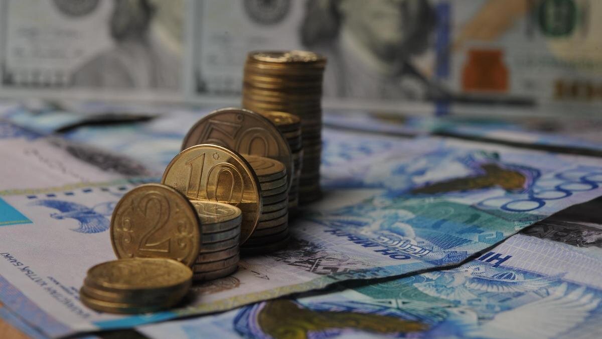   Стопки монет тенге стоят на фоне купюры доллара:NUR.KZ/Владимир Третьяков