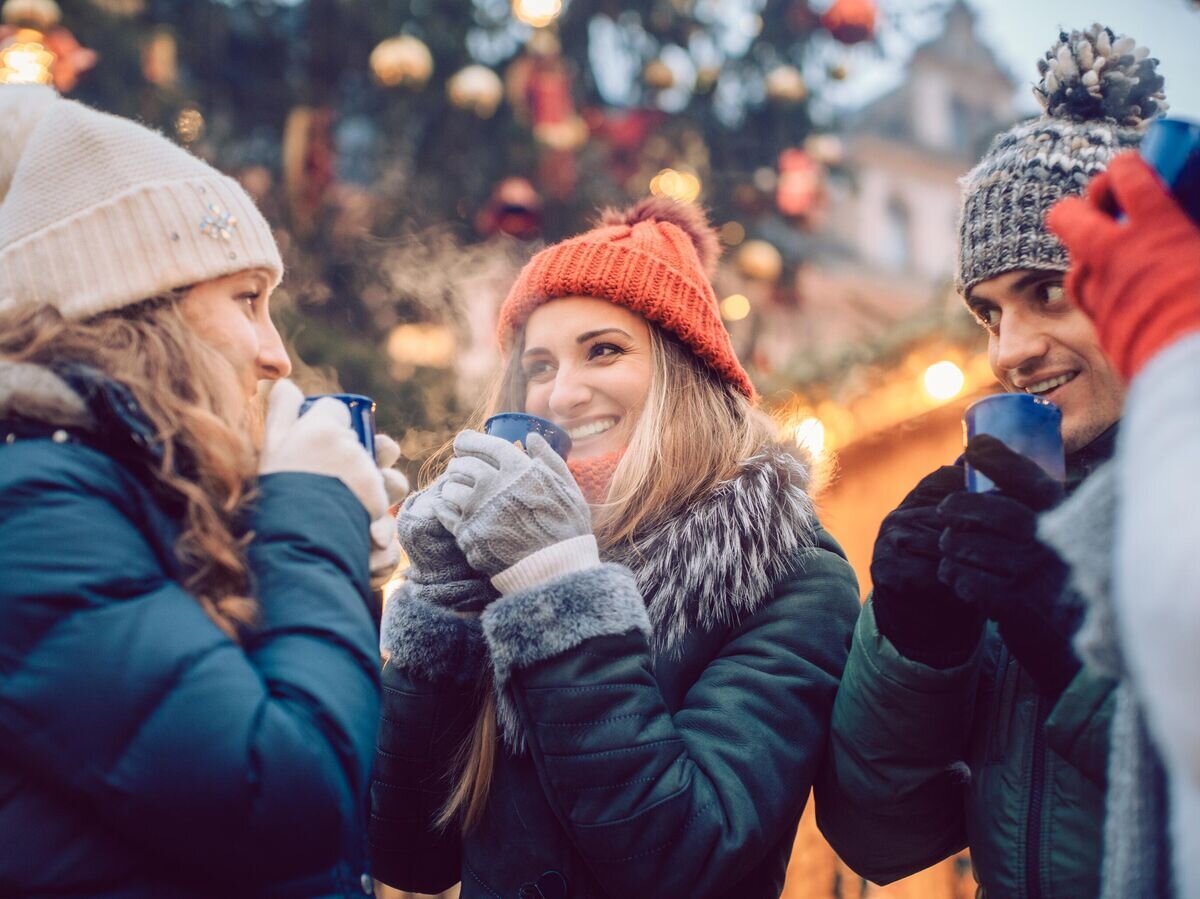    Друзья пьют глинтвейн на рождественской ярмарке © iStock.com / kzenon