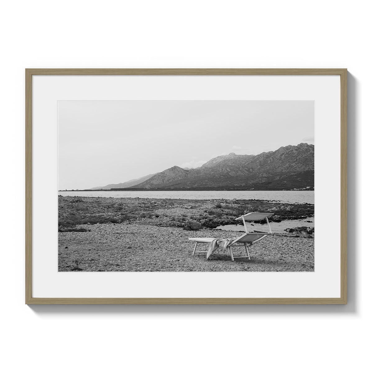 Черно-белая картина хорватской природы: морской залив с каменистым берегом, в левом нижнем углу одинокий шезлонг, словно ждущий своего путешественника. Горы, напоминающие альпийские вершины, создают мистическую атмосферу в этом пейзаже, переплетаясь с бескрайней красотой природы Хорватии. 