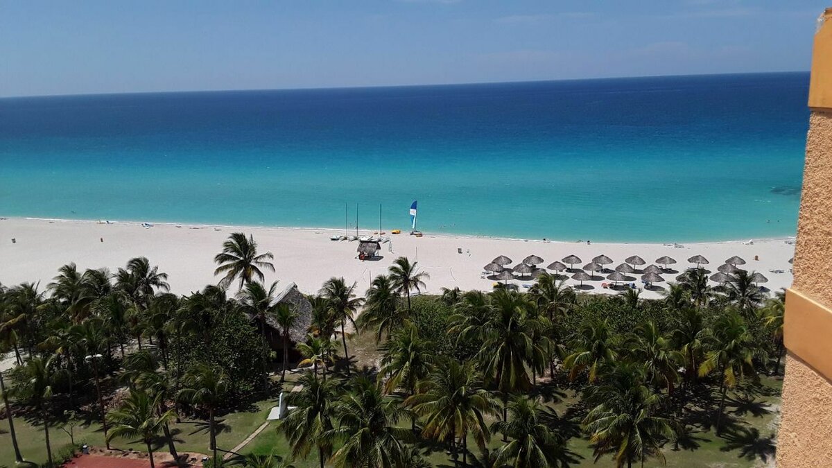 С высоты номера отеля песок кажется совсем белым, а океан — бирюзовым. Справа, где зонтики, территория гостиницы. Фото: Надежда Боровикова