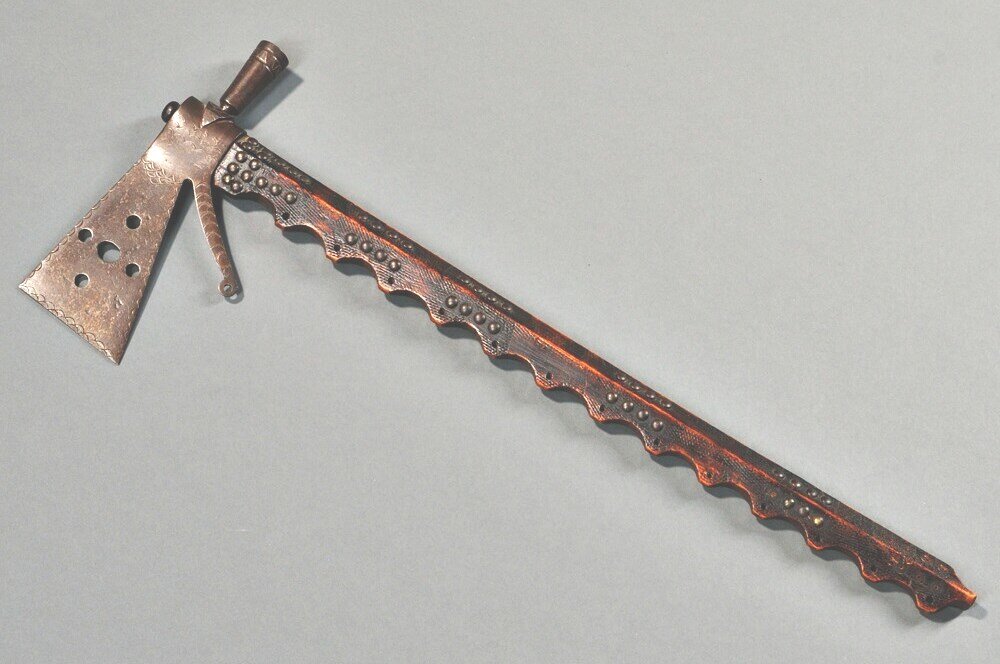 Great Lakes Tomahawk, c. last quarter 19th century, the head with perforations, incised decoration, and elaborate sword guard, the file-branded ash haft scalloped and perforated down one side, further decorated with metal tacks, dark patina, (some tacks missing), lg. 25, lg. of head 10 in.