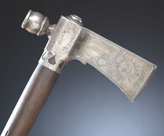 French Presentation Pipe Tomahawk pewter head, bands, and mouthpiece; blade heavily decorated with imagery of the moon, stars, sun, and fleur-de-lis; additional inscriptions of Hibou Pleurant/ Loyal en Taut (Crying Owl, Loyal in All) and Un Guerrier Brave 1765 (A Brave Warrior, 1765), overall length 20 in., blade length 6.5 in. A similarly decorated tomahawk dated 1760, is attributed to the Mohawk and published in Hartzler and Knowles (1995: 128, fig. 128). Cowans Oct 2019