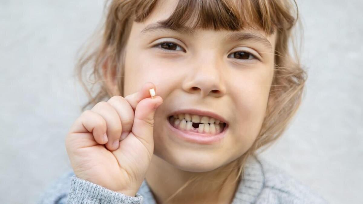    Девочка держит в руке выпавший молочный зуб:Freepik