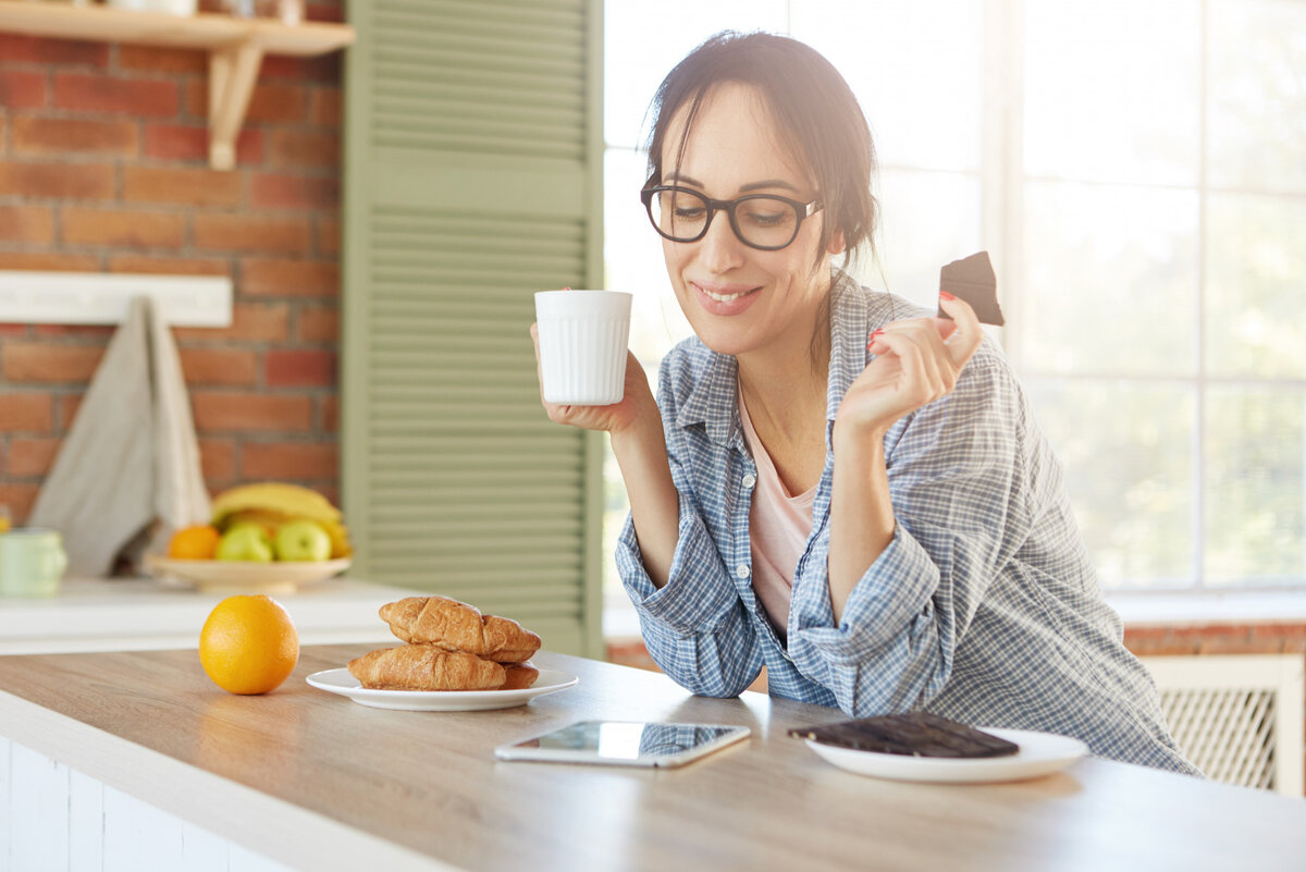 Женщина завтракает. Девушка в очках завтракает. Женщина пьет кофе с круассаном фото. Бизнес-леди кушает дома.