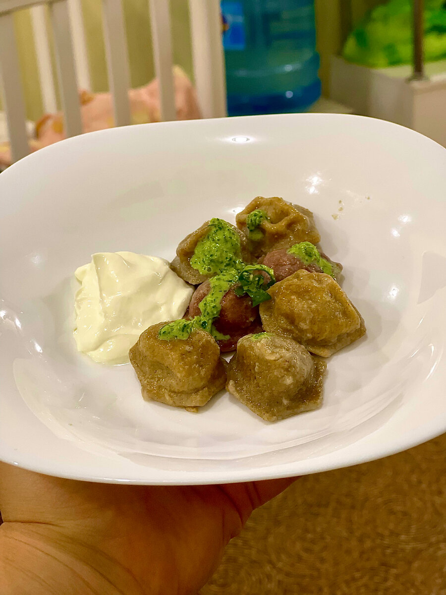 Пельмешки цветные украшены соусом из сметаны и зелени. 