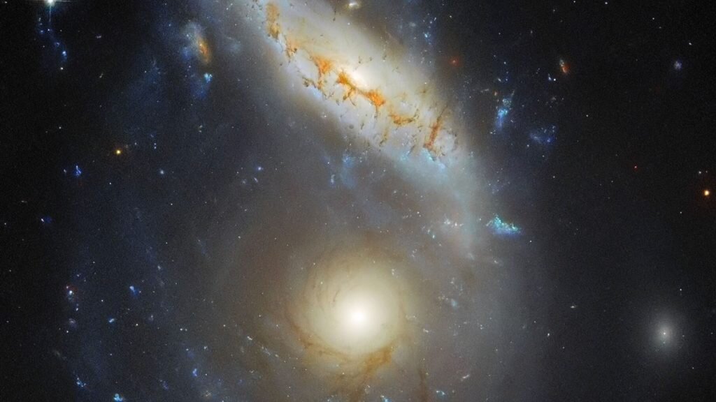    This Hubble Picture of the Week features Arp 122, a peculiar galaxy that in fact comprises two galaxies — NGC 6040, the tilted, warped spiral galaxy and LEDA 59642, the round, face-on spiral — that are in the midst of a collision. This dramatic cosmic encounter is located at the very safe distance of roughly 570 million light-years from Earth. Peeking in at the corner is the elliptical galaxy NGC 6041, a central member of the galaxy cluster that Arp 122 resides in, but otherwise not participating in this monster merger. Galactic collisions and mergers are monumentally energetic and dramatic events, but they take place on a very slow timescale. For example, the Milky Way is on track to collide with its nearest galactic neighbour, the Andromeda Galaxy (M31), but these two galaxies have a good four billion years to go before they actually meet. The process of colliding and merging will not be a quick one either: it might take hundreds of millions of years to unfold. These collisions take so long because of the truly massive distances involved. Galaxies are composed of stars and their solar systems, dust and gas. In galactic collisions, therefore, these constituent components may experience enormous changes in the gravitational forces acting on them. In time, this completely changes the structure of the two (or more) colliding galaxies, and sometimes ultimately results in a single, merged galaxy. That may well be what results from the collision pictured in this image. Galaxies that result from mergers are thought to have a regular or elliptical structure, as the merging process disrupts more complex structures (such as those observed in spiral galaxies). It would be fascinating to know what Arp 122 will look like once this collision is complete . . . but that will not happen for a long, long time.  [Image Description: Two spiral galaxies are merging together at the right side of the image. One is seen face-on and is circular in shape. The other seems to lie in fron Александр Шереметьев
