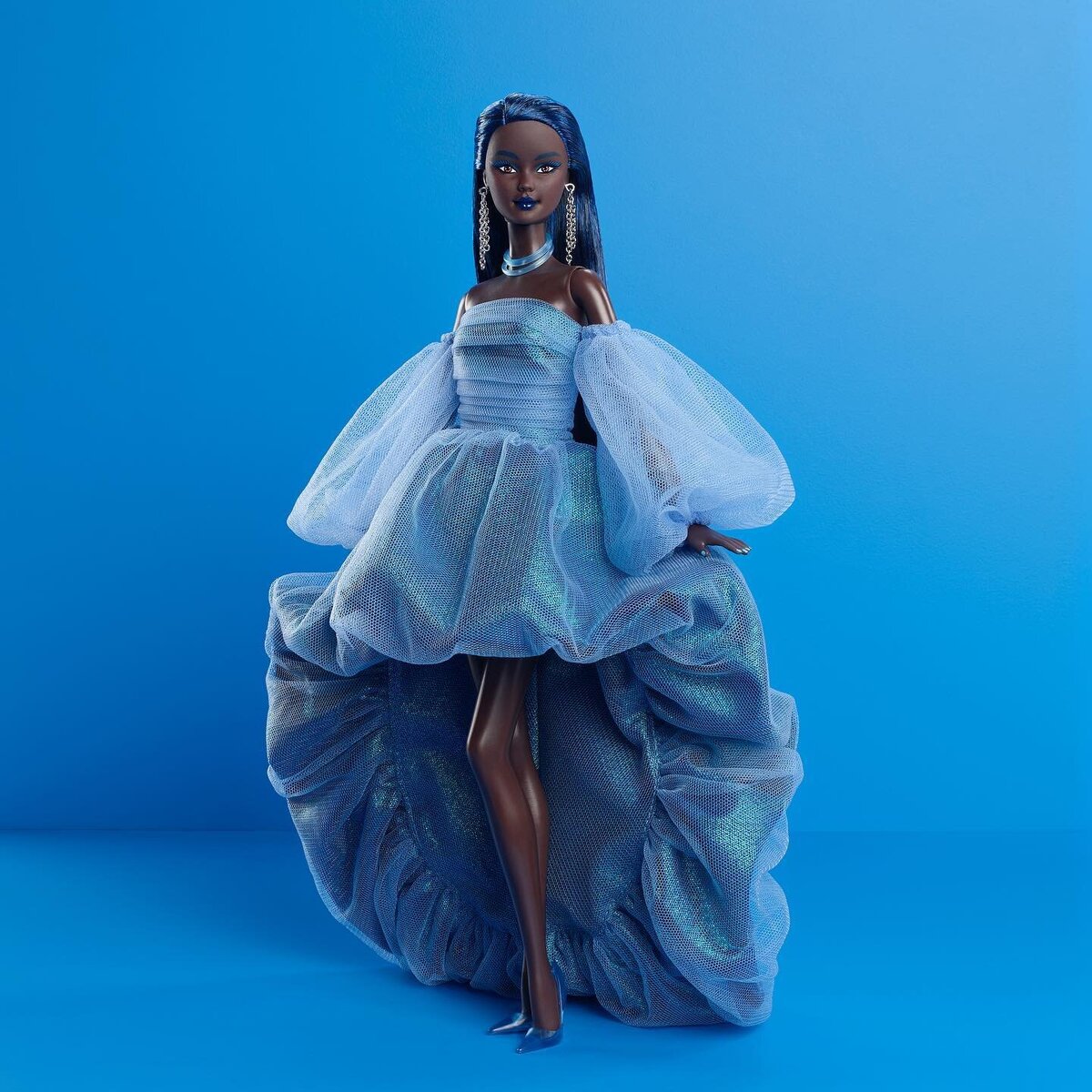 Chromatic Couture Barbie Blue облачена в полностью синий ансамбль, соответствующий ее тотемному цвету: волосы цвета electric-blue, обрамляющие ее черную кожу, деликатно подчеркнутую синим макияжем. Наряд включает в себя серьги-цепочки, синее ожерелье и кольцо, струящееся синее платье и соответствующие синие туфли на каблуке с ремешками.