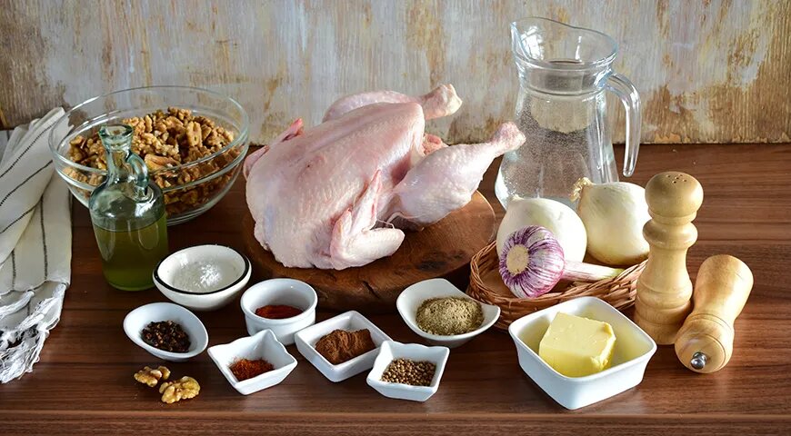 Раскладка продуктов для сациви. Суповая курица, грецкие орехи, семена кориандра, шафран и уцхо-сунели, белый лук, чеснок, сливочное масло, кукурузный крахмал, белый винный уксус, вода для бульона, соль, свежемолотый черный перец, красный молотый чили, молотая корица и молотая гвоздика