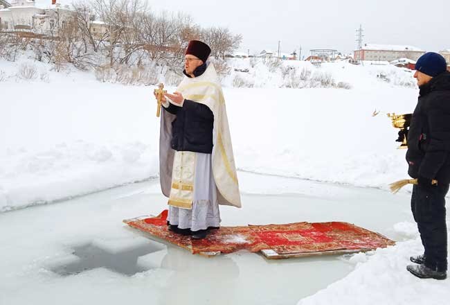 Священник Максим Кулаков освящает воду на Сылве в иордани, вырезанной во льду