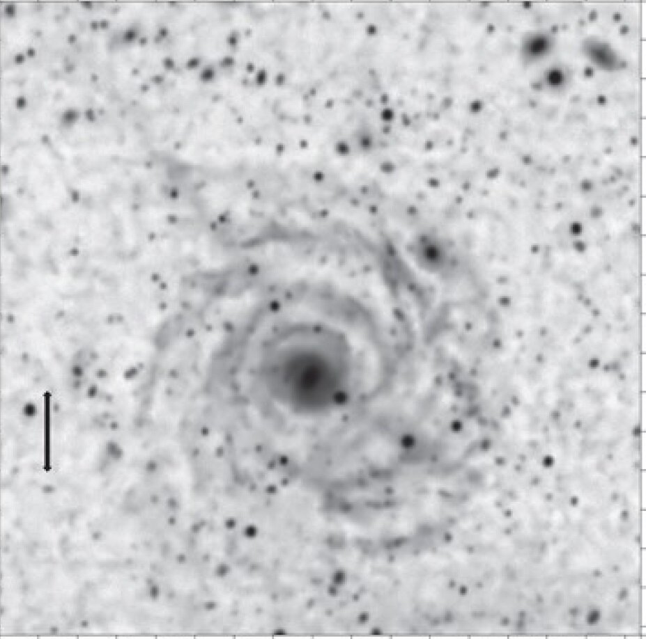 Рис. 1. Галактика с низкой поверхностной яркостью Malin 1. Размер стрелка слева равен размеру нашей Галактики – примерно 100 тысяч световых лет. Диаметр галактики Malin 1 примерно в 7 раз больше. Но её яркость очень низка – изображение было получено с экспозицией 4.5 часа. (Изображение из статьи G. Galaz с соавторами, 2015, Astrophys. J. Letters, Dec20) 