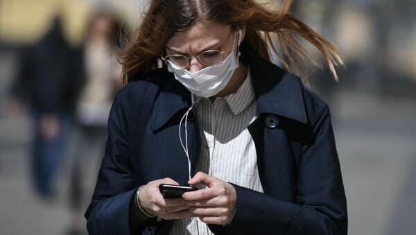    Девушка в маске смотрит в телефон / © ria.ru