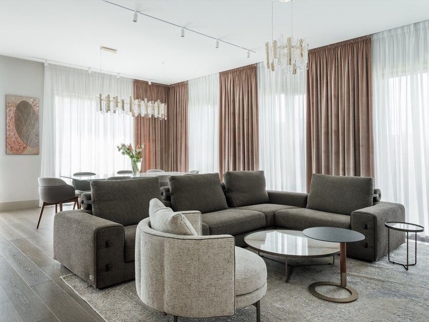 Зона гостиной. На полу — инженерная доска кофейно-серого оттенка, изготовленная на заказ под цветовую гамму интерьера компанией Finex. Диван, Gamma. Кресло, Minotti. Журнальные столики, Cattelan Italia, Porada. Обеденная группа, Bonaldo. Люстры над обеденным и журнальными столами, IDL. Картина, Дмитриева Дарья, галерея SMART.