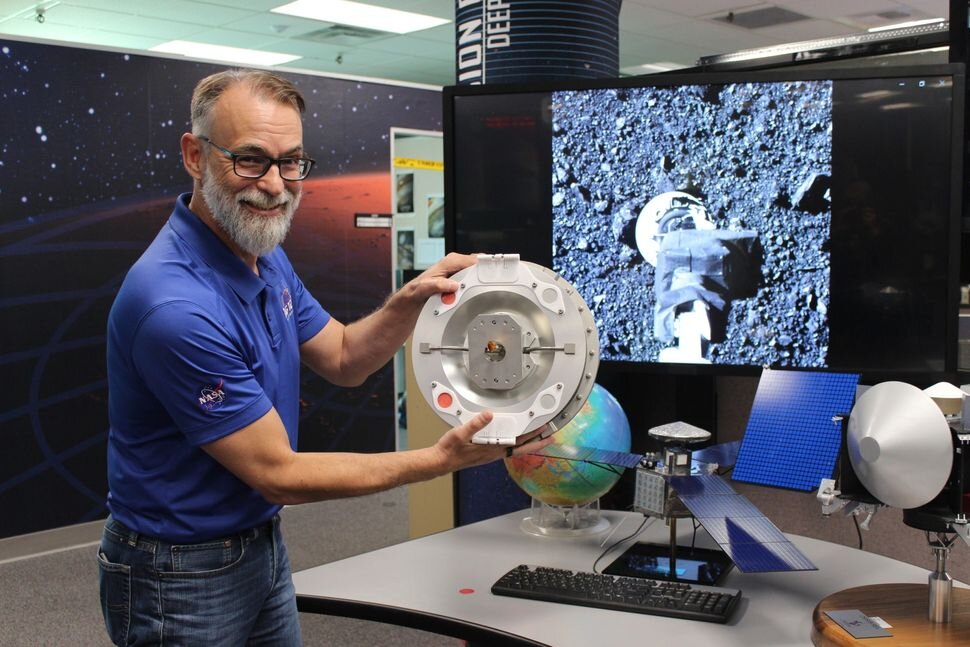 Данте Лауретта, главный исследователь OSIRIS-Rex из Университета Аризоны, держит в копию устройства для сбора образца с астероида Бенну, верхнюю часть механизма сбора образцов TAGSAM.    
 Источник: Barbara David  📷
