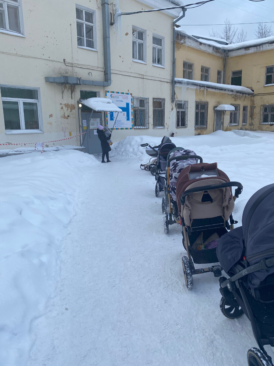 Парковка из колясок вдоль небольшой тропинки. Остальная территория перед больницей вся в снегу.