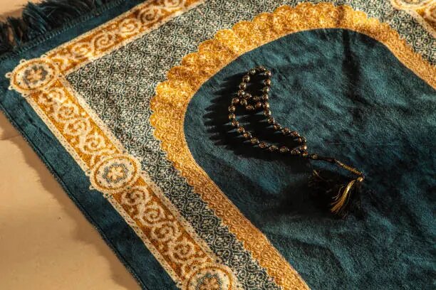    prayer beads and Holy Noble Quran Book with Calligraphy leather cover on a Decorated Praying Carpet with Natural Light rays press.kz