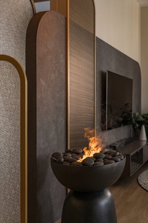 Центральный элемент декора гостиной — стеклянные перегородки из узорчатого закаленного стекла в металлической раме, изготовленные по проекту дизайнеров компанией «ЛидерГласс». Уюта прохладными вечерами добавляет электрический паровой камин Dimplex, встроенный в отдельно стоящий постамент, изготовленный в мастерской Анны Норец.