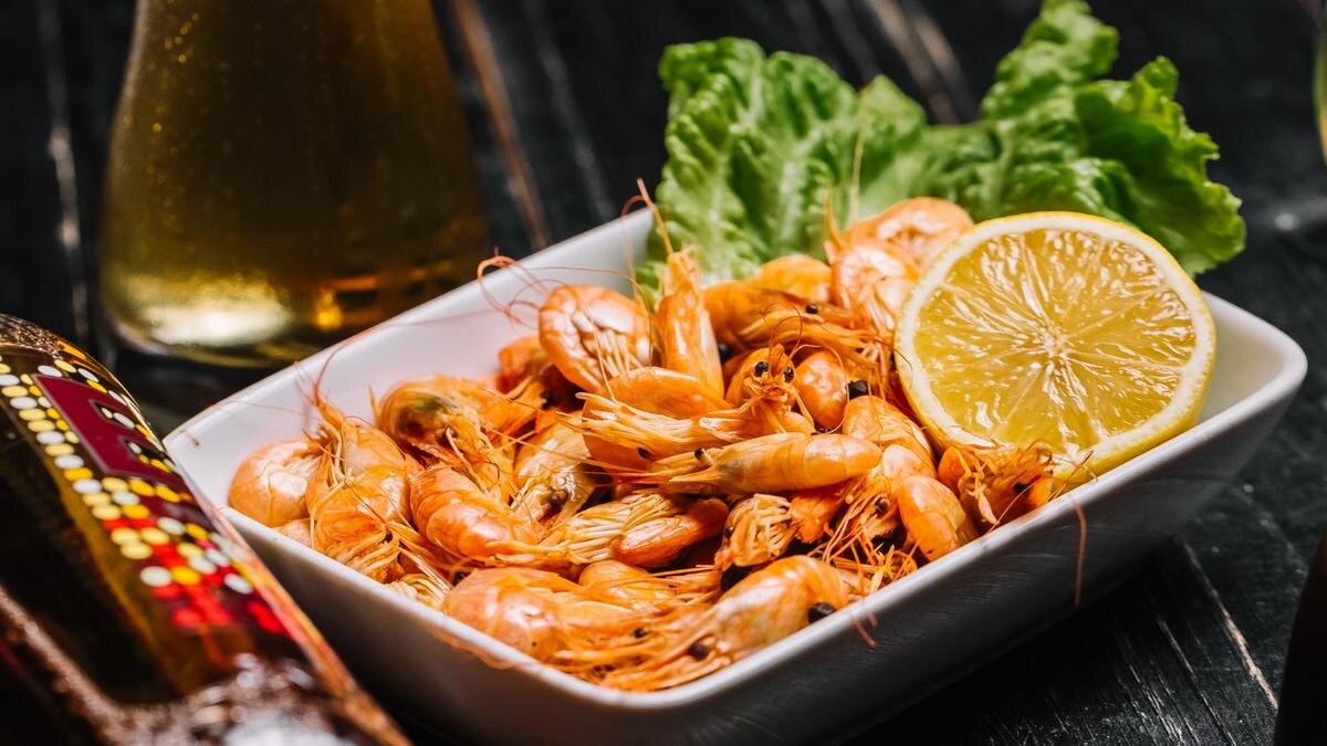    В прямоугольной тарелке мелкие креветки с лимоном и листом салата:Freepik