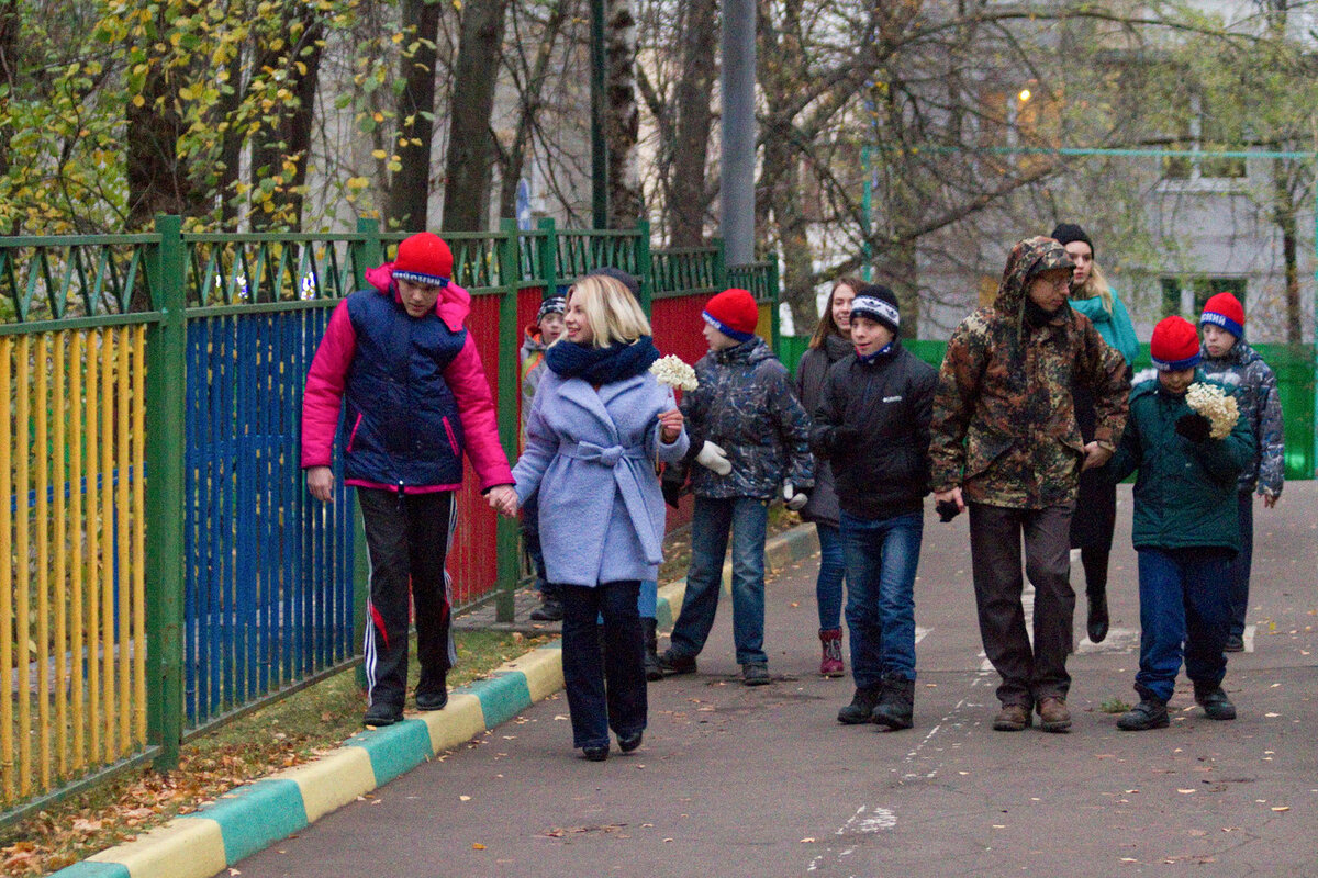 Рост Димы – меньше метра. Поэтому волонтёрка садится рядом с ним на корточки и высоко поднимает шишку. Разжимает пальцы, шишка падает на асфальт. Дима внимательно следит за ней глазами.-3