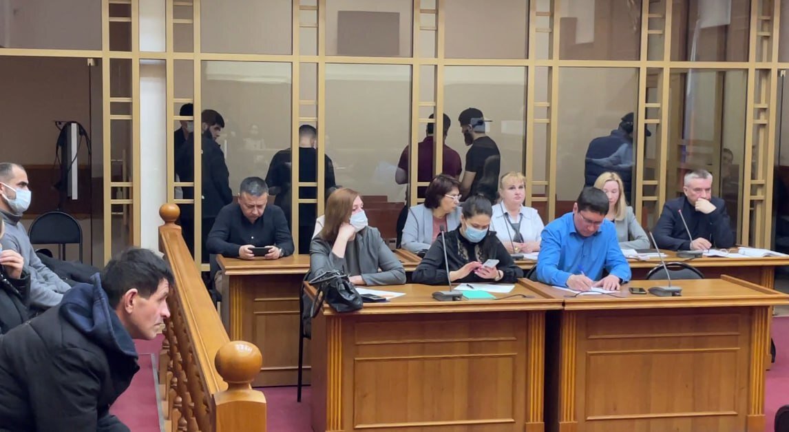 Перед решетчатой кабиной для подсудимых в два ряда стоят столы для адвокатов и переводчиков. Потерпевшую сторону представляет гособвинитель. На первое заседание семья русского парня не пришла. Фото: Царьград.