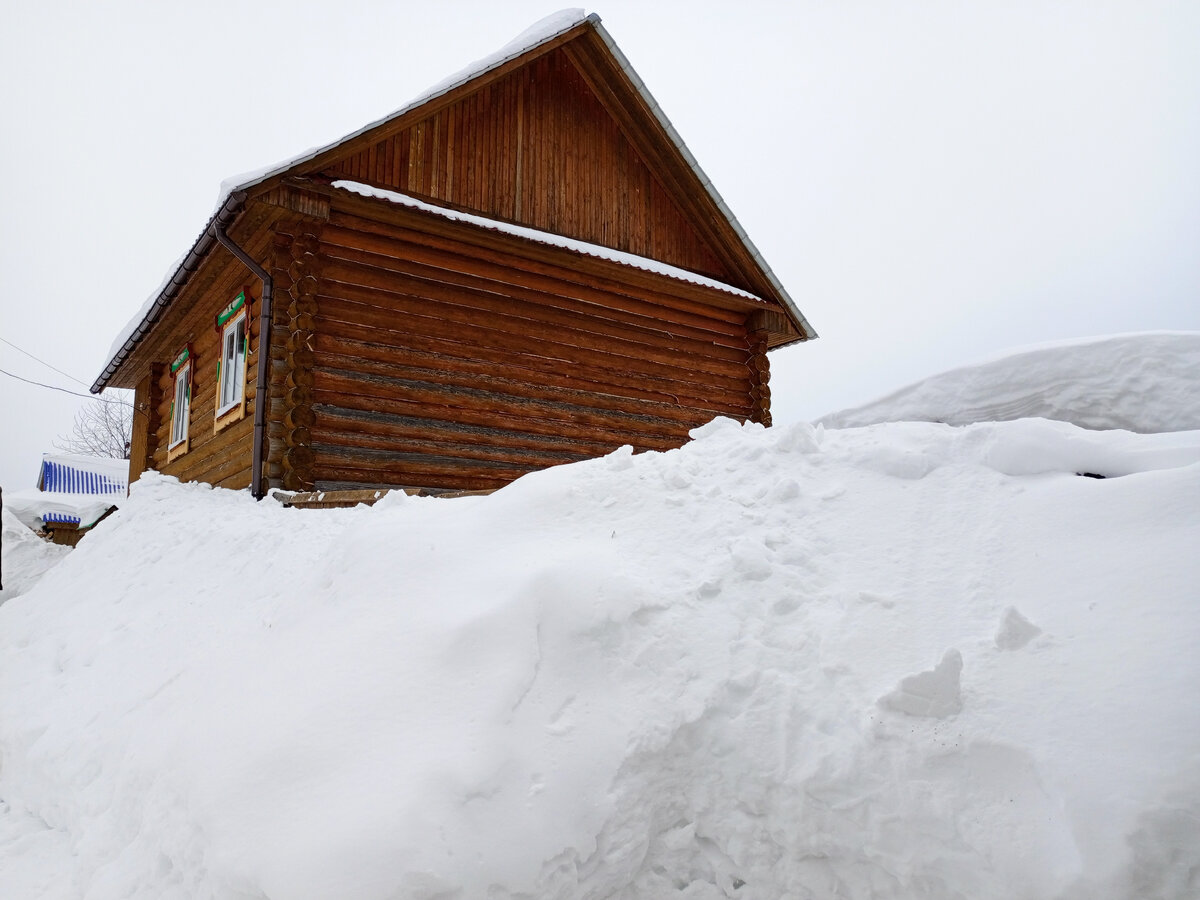Большие сугробы достают почти до крыши 2-этажного деревянного срубленного дома. Фото автора.