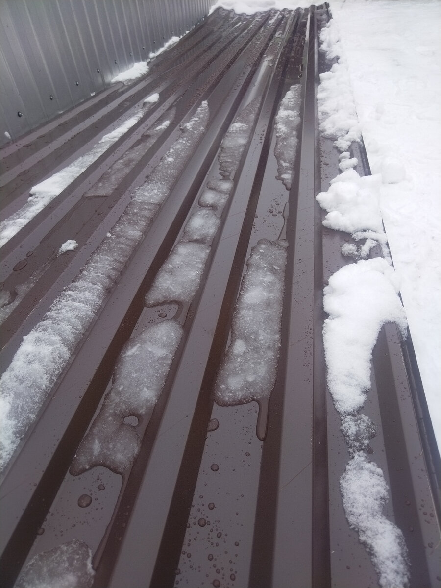  Видно, как выпавший снег тает на коричневых волнах кровельного профлиста.