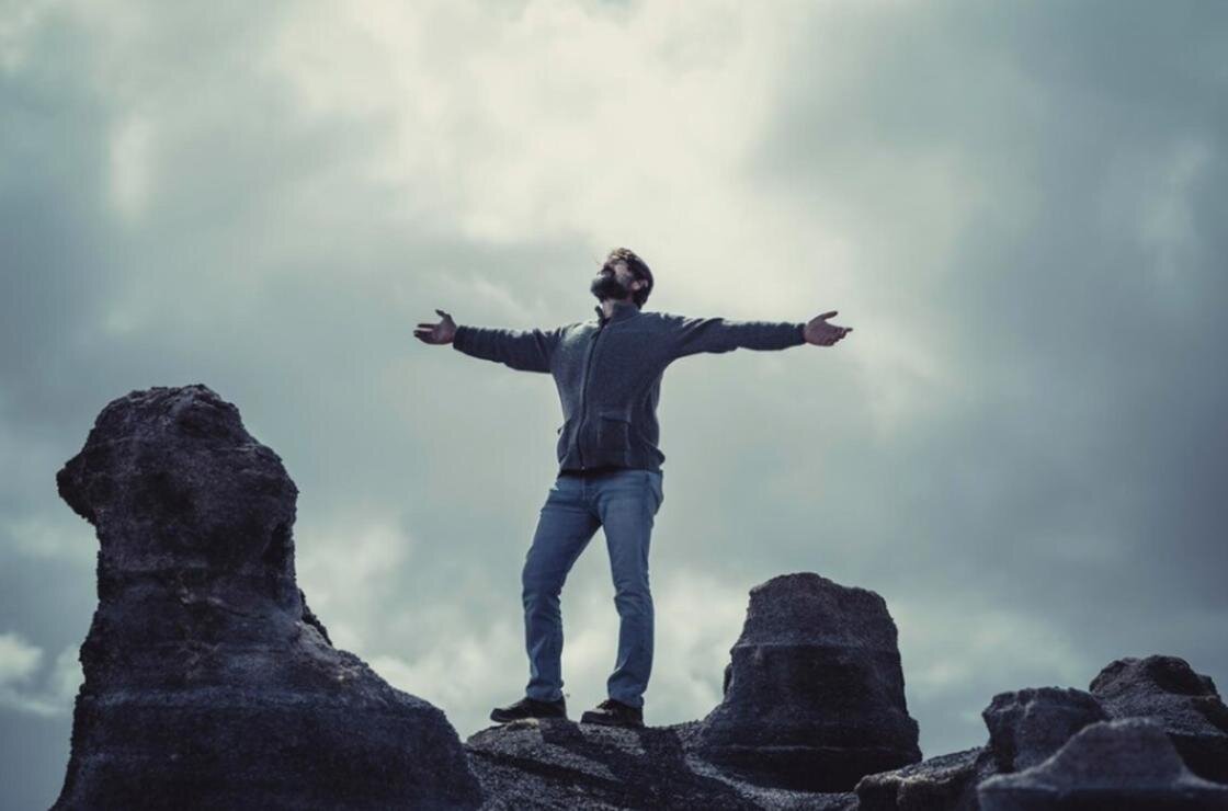    Мужчина стоит на скале с раскинутыми в стороны руками:Freepik