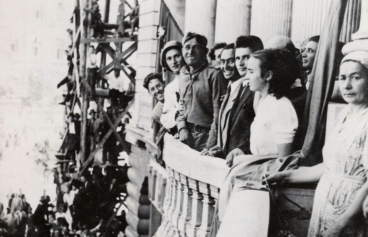 Николае (в черном пиджаке) и Елена Чаушеску (в белой блузке) на балконе с видом на Университетскую площадь Бухареста. Они приветствуют прибытие советских войск в Румынию после свержения профашистского режима в августе 1944 года.