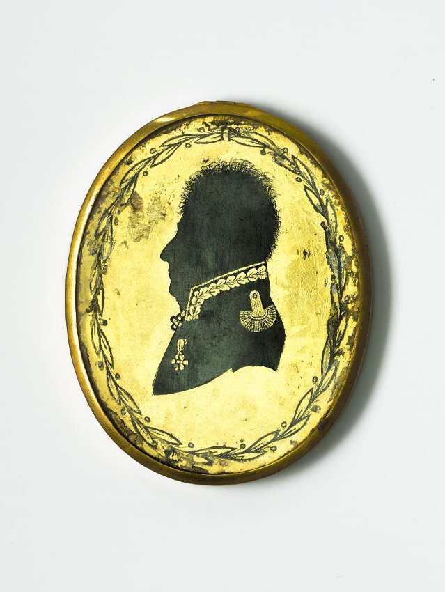 Медальон. Россия, конец XVIII в. Высота: 6 см; ширина: 4,8 см. На медальоне — погрудный портрет пожилого мужчины. Мужчина в мундире со стоячим воротником, украшенным дубовыми листьями, с эполетом на плече, орденами на груди и на шее. На оборотной стороне — вензель «СГ» на зеленом фоне. Оправа гладкая, золоченая, украшена сканью в виде сдвоенных завитков.